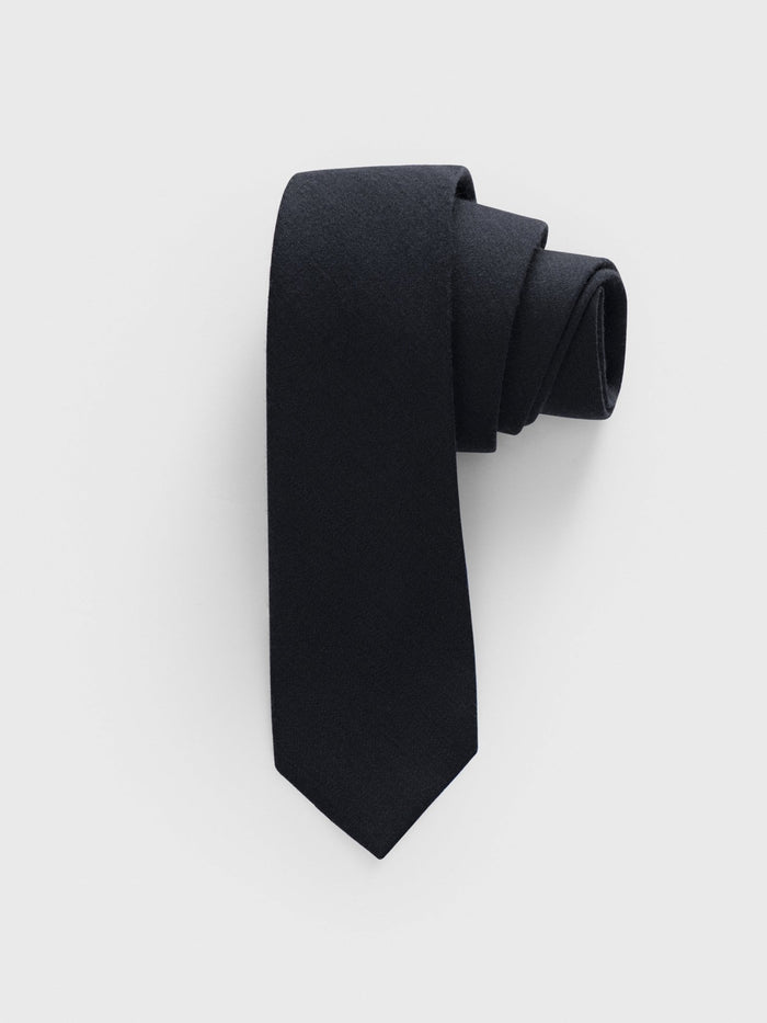 Black necktie rolled into a coil on a grey background.