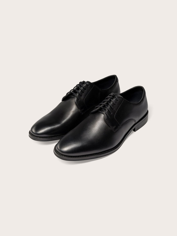 A pair of black leather dress shoes with laces on a light background.
