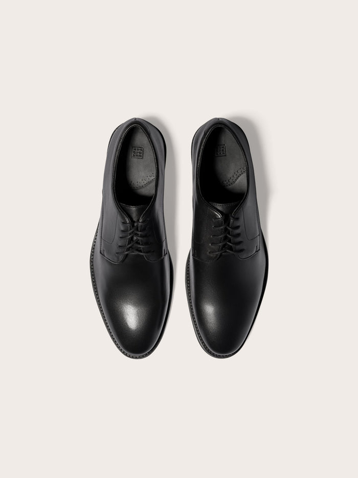 Pair of black leather lace-up dress shoes, top-down view, cream background.