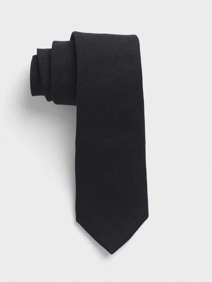 Black linen necktie rolled into a coil on a grey background.