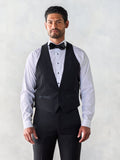 Man in a black low-cut tuxedo vest with white shirt and black bow tie, grey backdrop.