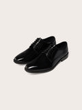 Pair of black patent leather lace-up dress shoes, cream background.
