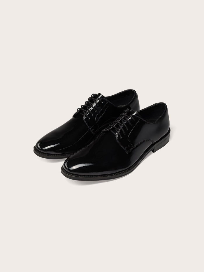 Pair of black patent leather lace-up dress shoes, cream background.
