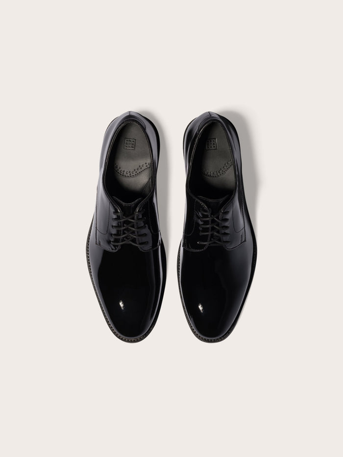 Black patent leather dress shoes with laces, top-down view, cream background.