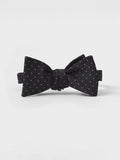 Black silk bow tie with white pindots, tied, on a grey background.