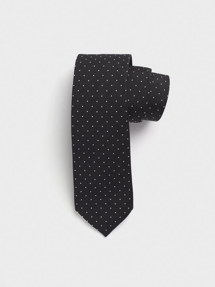 Black silk necktie with white pindots, rolled up on a grey background.