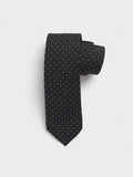 Black silk necktie with white pindots, rolled up on a grey background.