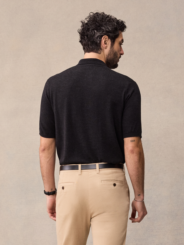 Man in a black short-sleeve sweater polo, back view, beige backdrop.