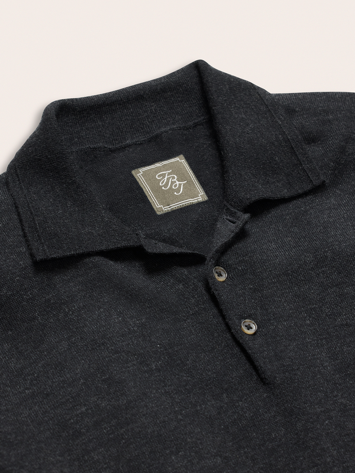 Close-up of black sweater polo collar and button placket with brand tag.