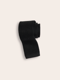 Black silk knit tie rolled into a coil on a cream background.