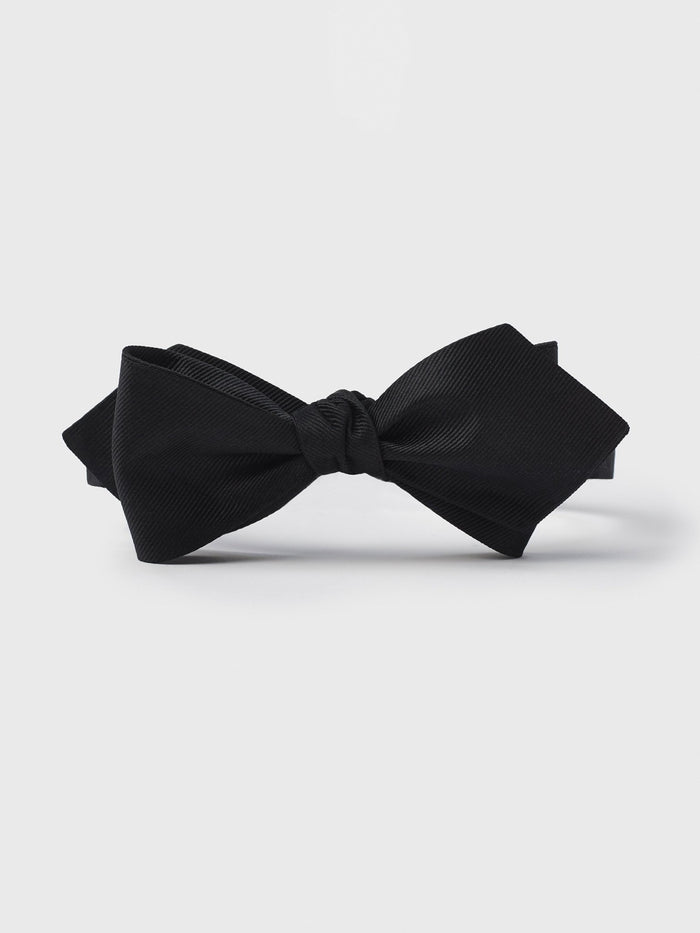 Black silk twill diamond-point bow tie, tied, on a grey background.