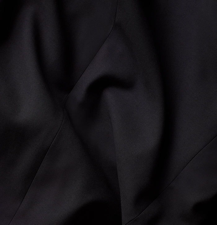 Close-up of black suit trouser fabric, draped to show texture.