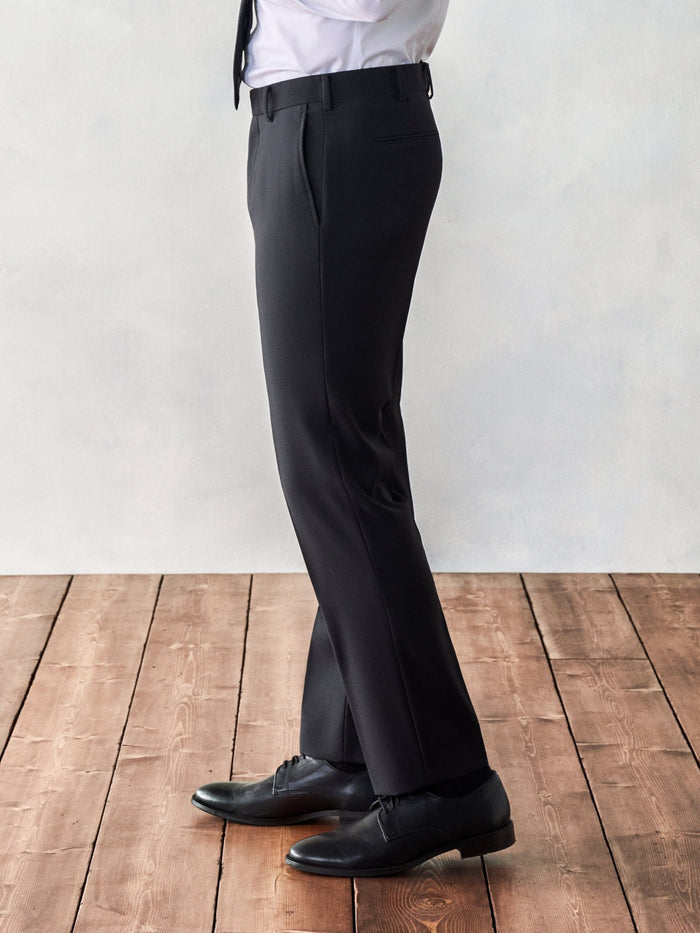Side view close-up of black suit trousers, wood floor backdrop.
