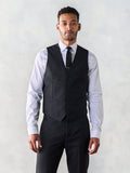 Man in a black suit vest with white shirt and black tie, grey backdrop.