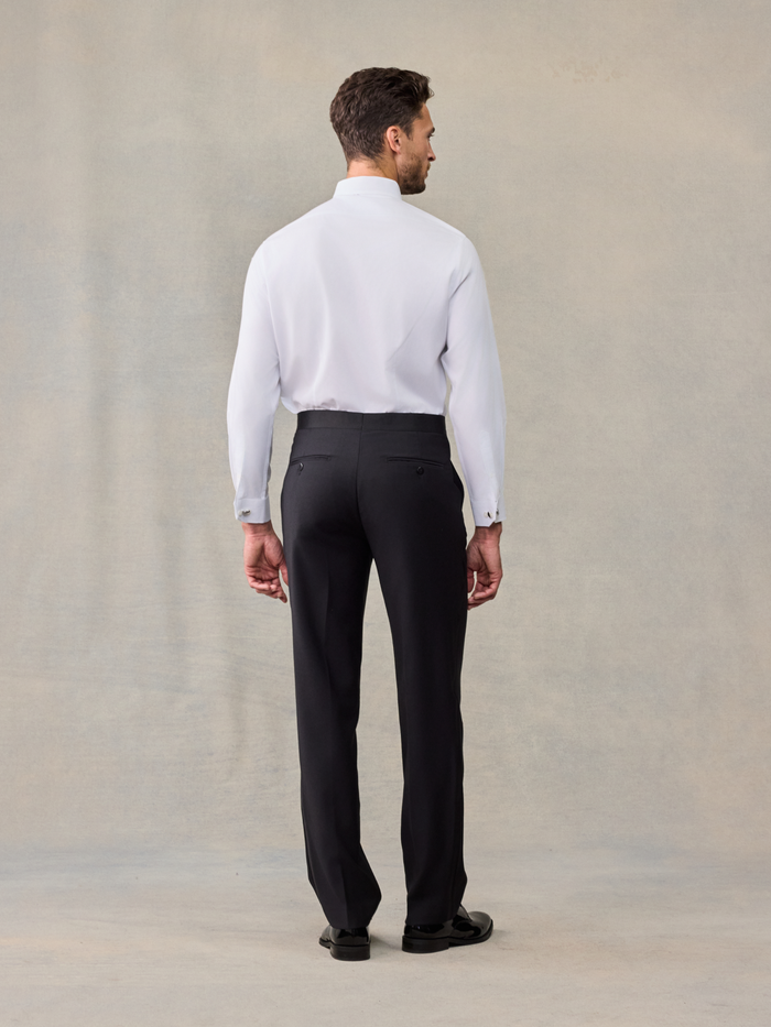 Back view of man in white tuxedo shirt and black trousers on beige backdrop