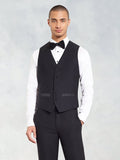 Man in a black tuxedo vest with black bow tie and white shirt, grey backdrop.