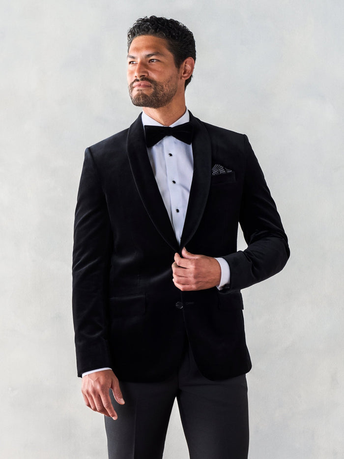 Man in a black velvet tuxedo jacket with shawl lapel, black bow tie, grey backdrop.