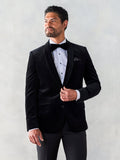 Man in a black velvet tuxedo jacket with shawl lapel, black bow tie, grey backdrop.