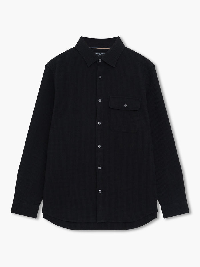 A man wearing a black regular fit shirt with long sleeves, a pointed collar and button down fastening.