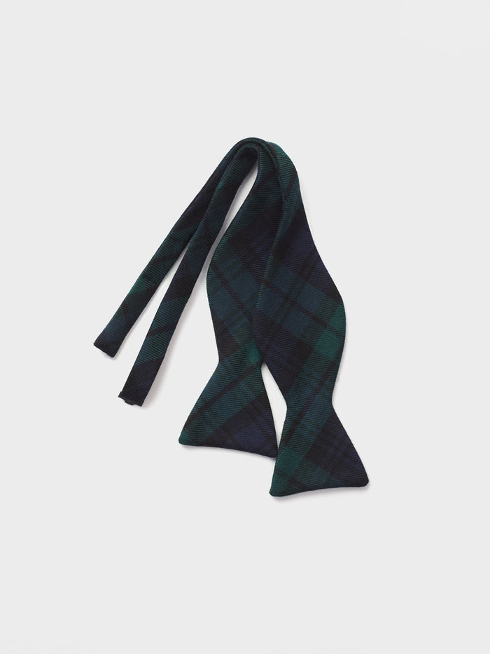 Untied black watch tartan bow tie draped on a grey background.