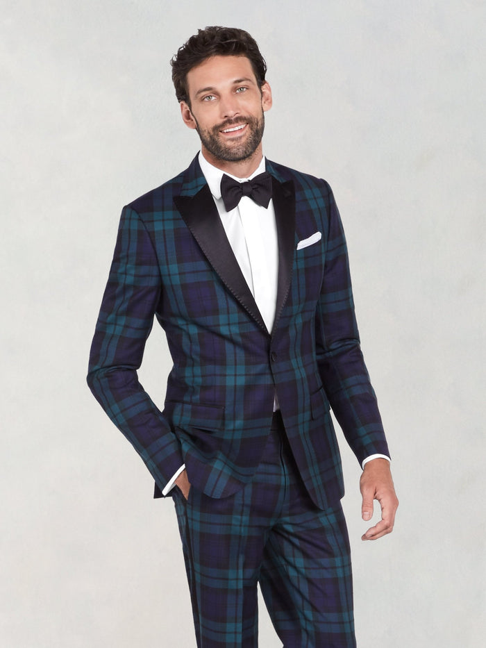 Man in a black watch tartan tuxedo with black bow tie and satin lapels, grey backdrop.