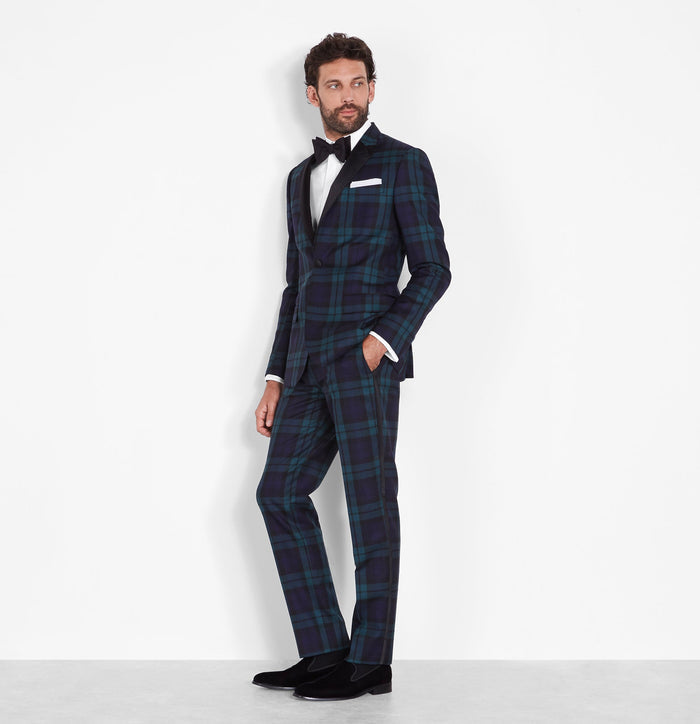 Man in a black watch tartan tuxedo, three-quarter view, hand in pocket, white background.