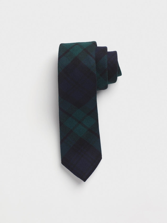 Black watch tartan wool necktie rolled into a coil on a grey background.