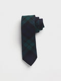 Black watch tartan wool necktie rolled into a coil on a grey background.