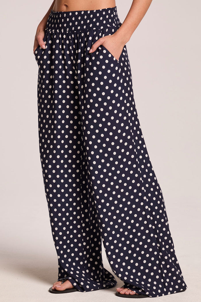 Side angle view of a woman wearing the Chaser Blair Navy Spot Trouser on a neutral background with hands in her pockets