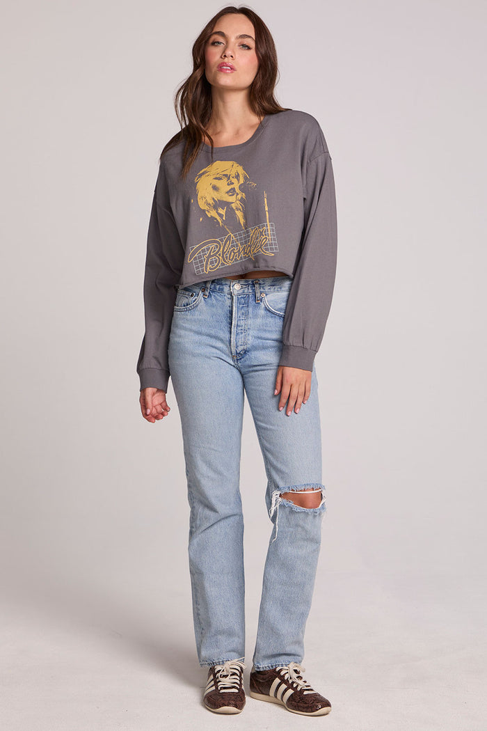 Full body view of a woman wearing the Chaser Blondie Live Cropped Sweatshirt on a neutral background with hands at sides and jeans