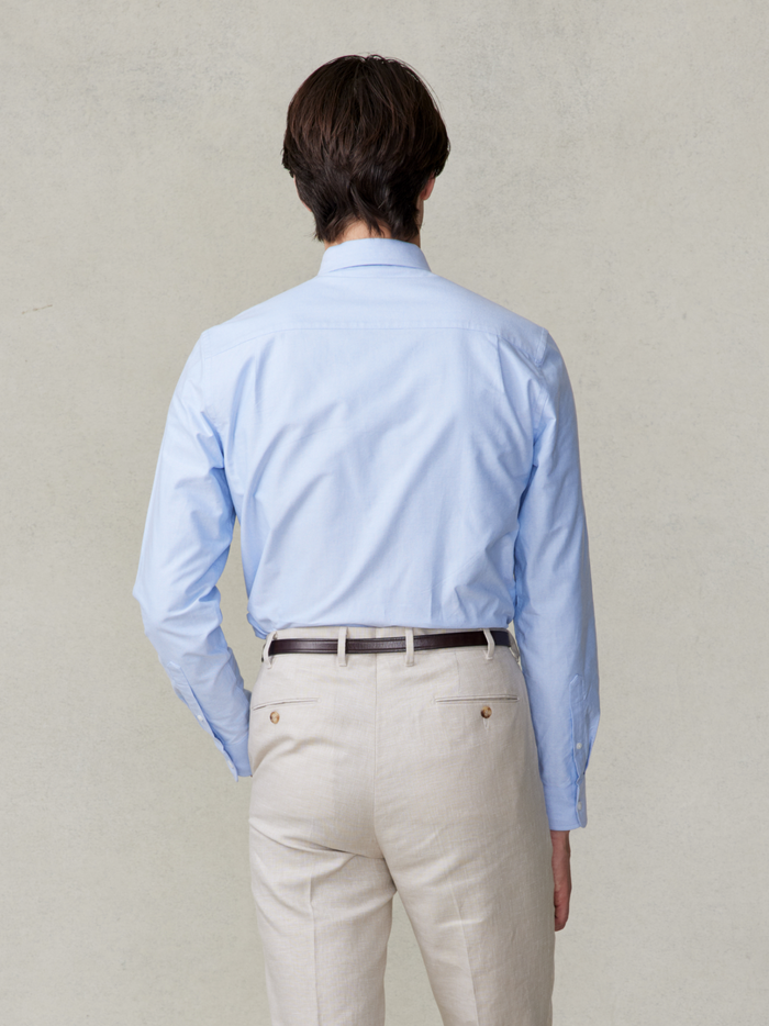 Cropped back view of a man in a light blue oxford shirt and tan trousers.