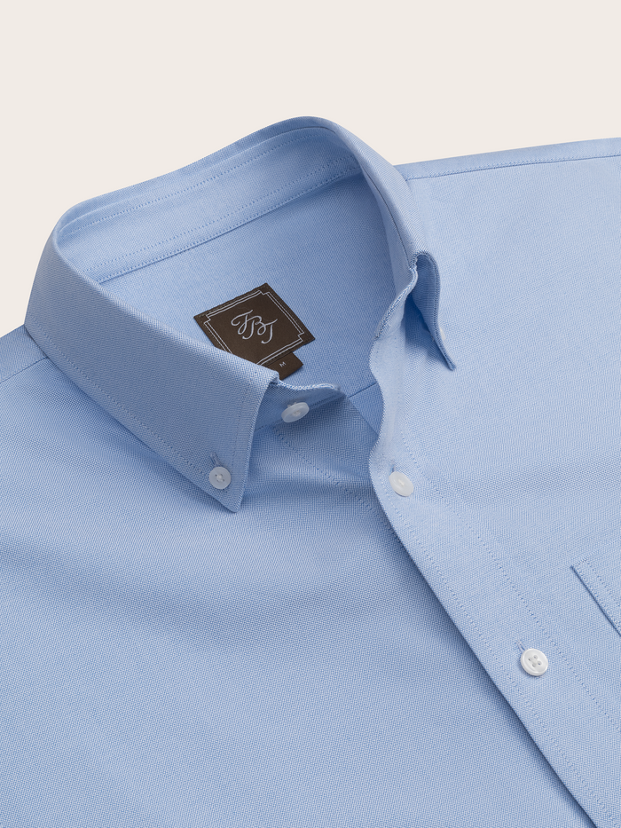 Close-up of a light blue oxford shirt's button-down collar and brand tag.