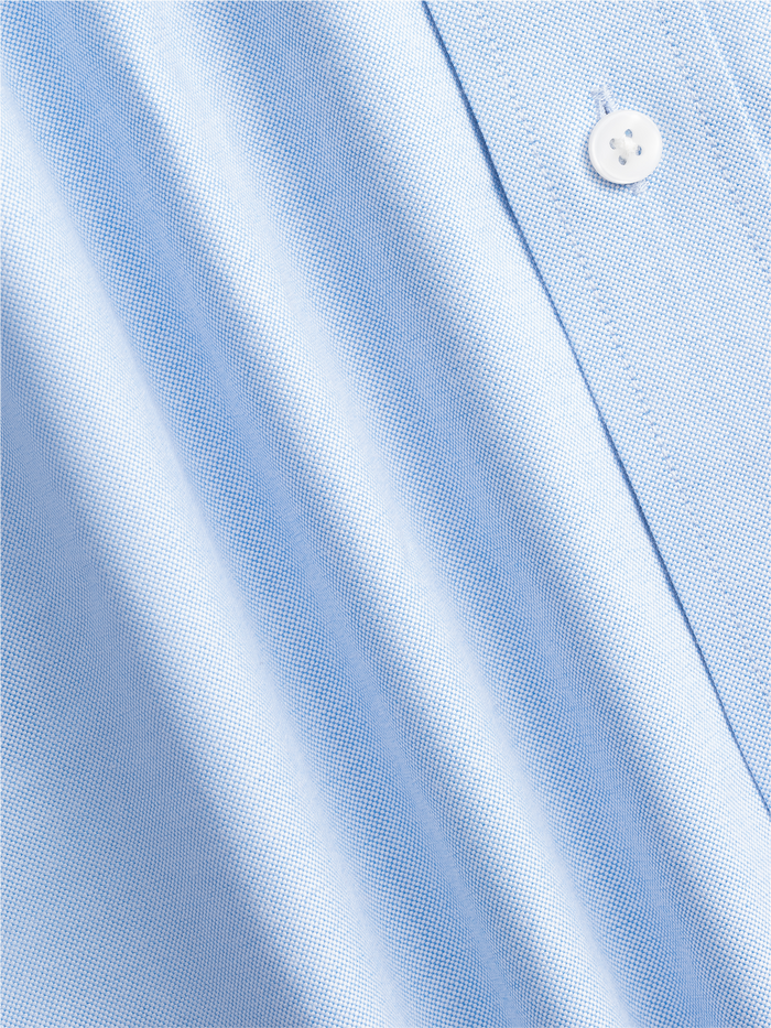Close-up of light blue oxford shirt fabric with a white button and stitched seam.