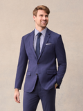 Man in a blue suit with striped shirt, navy tie, and pocket square, hand in pocket