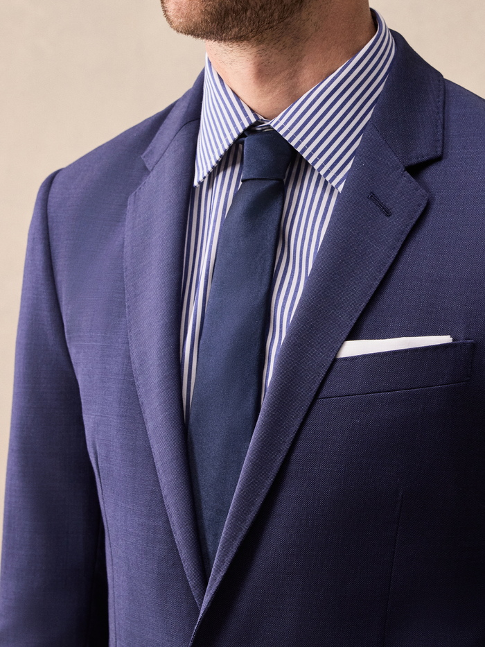 Close-up of a blue suit lapel with striped shirt, navy tie, and white pocket square