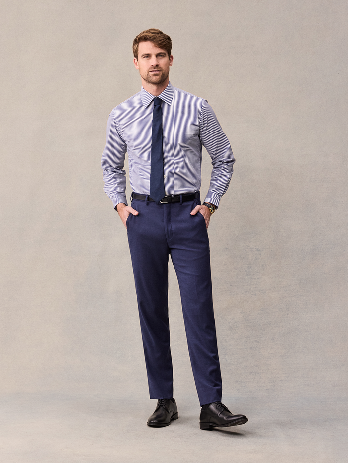 Man in a blue and white striped shirt and navy tie with blue suit trousers, no jacket, front view.