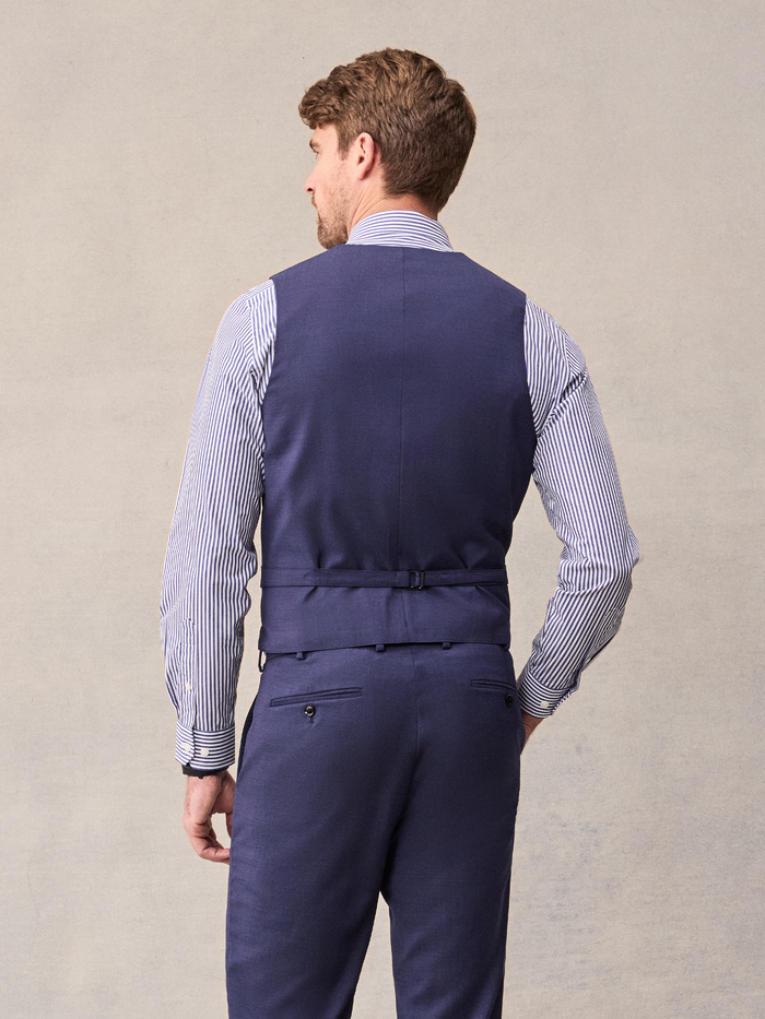 Cropped back view of a man in a blue suit vest with a back strap and striped shirt sleeves.
