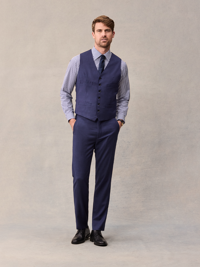Man in a blue suit vest, blue and white striped shirt, and navy tie, full-length front view.