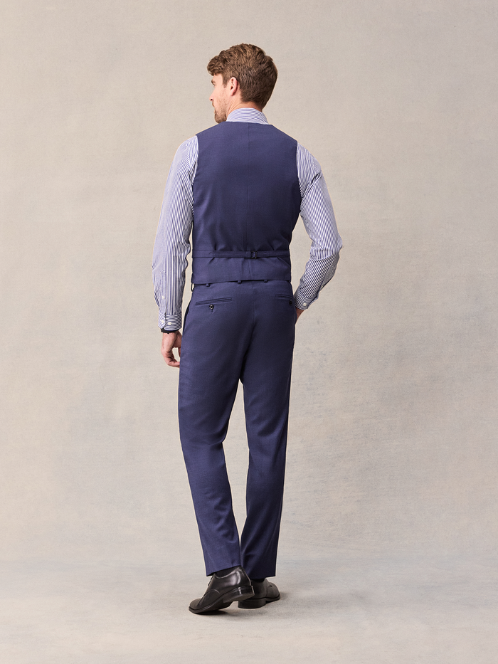 Back view of a man in a blue suit vest and trousers, full-length.
