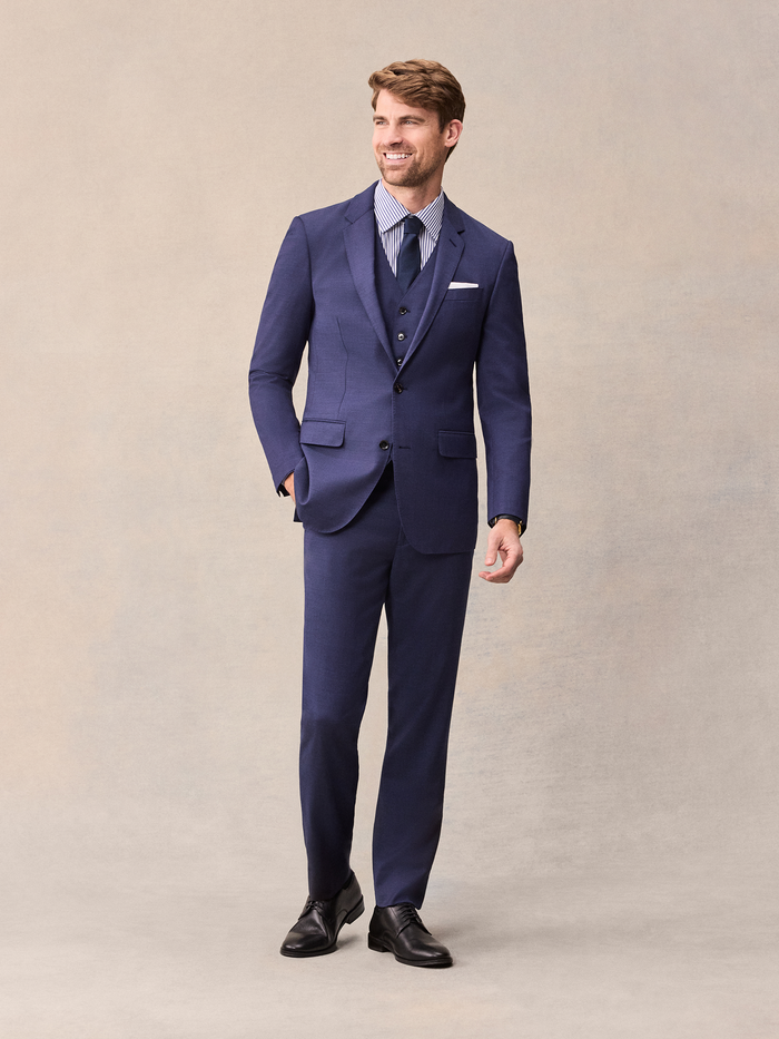 Man in a blue three-piece suit with vest, striped shirt, and navy tie, full length