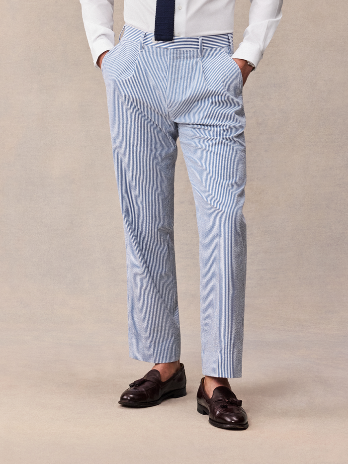 Cropped front view of a man in blue and white striped seersucker trousers and brown loafers.