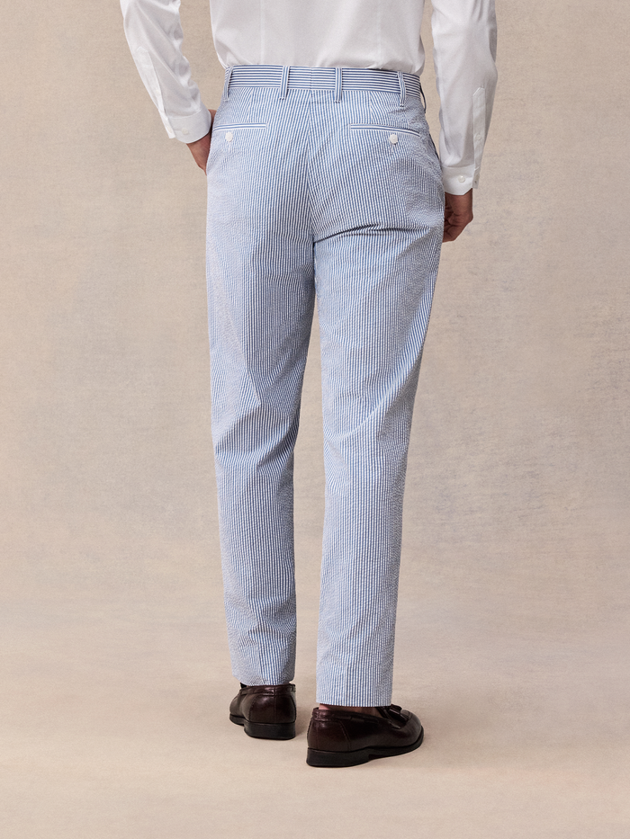 Cropped back view of a man in blue and white striped seersucker trousers and brown loafers.