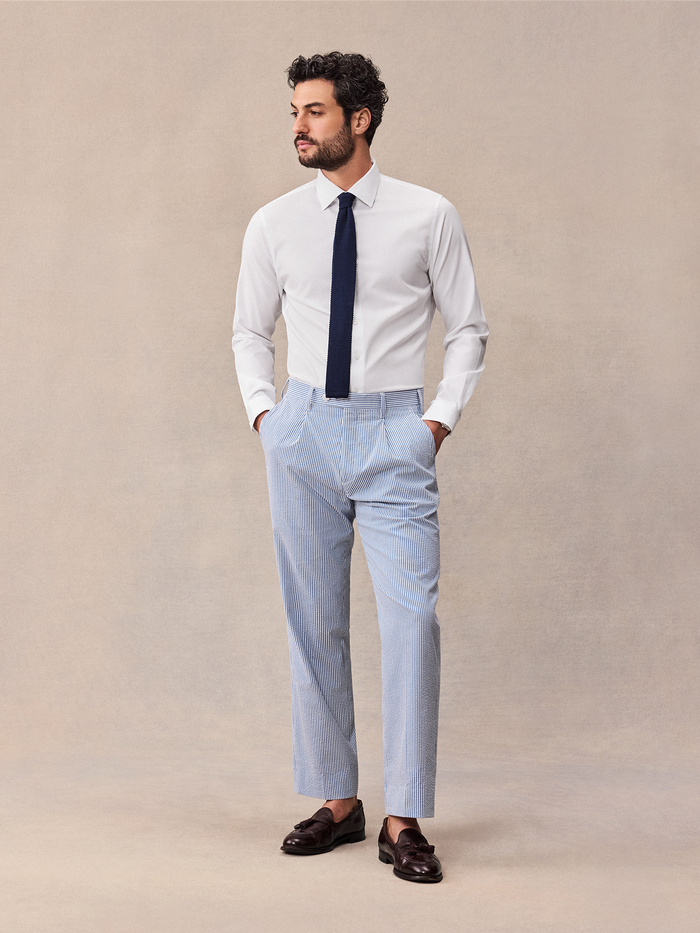 Man in white dress shirt and navy tie wearing blue and white striped seersucker trousers.