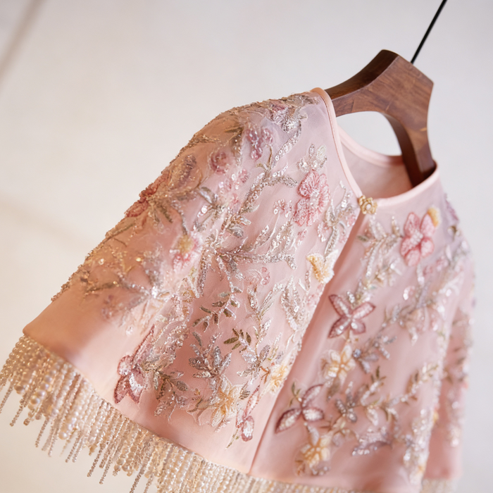 Blush pink bridal capelet featuring floral embroidery, sequins and hand beaded pearl fringe on soft illusion tulle.
