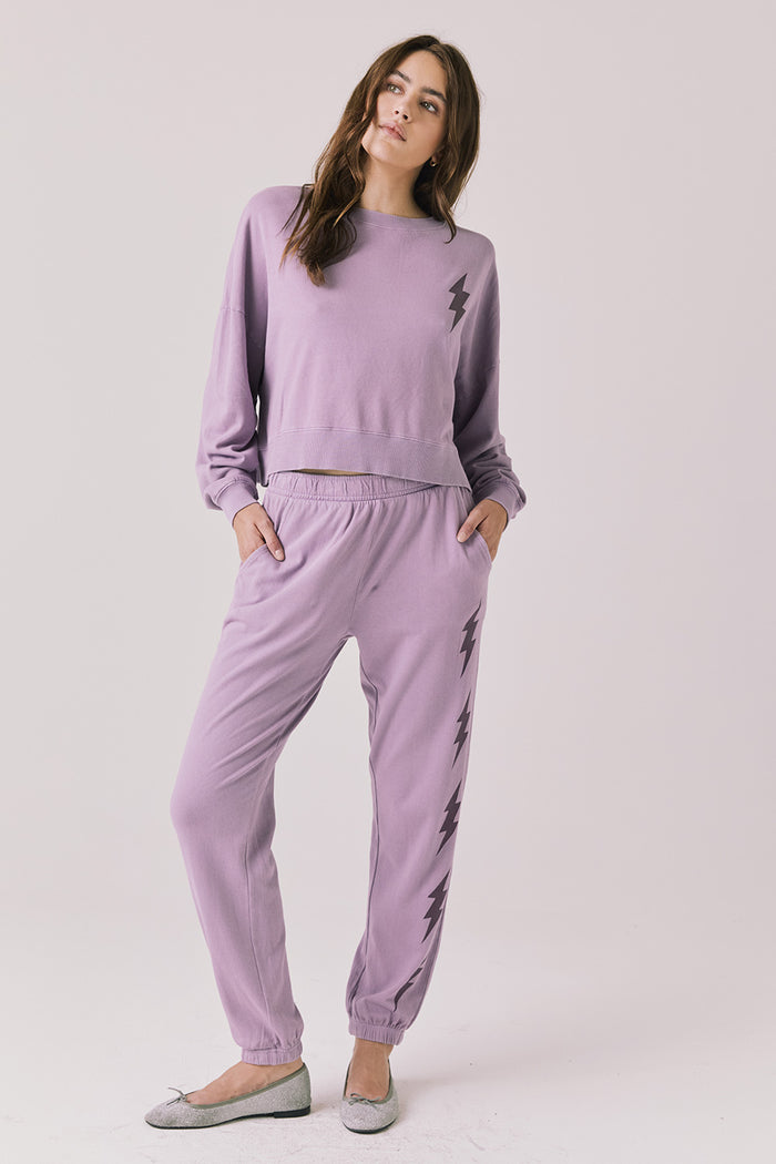 Full body view of woman wearing Chaser’s Bolt Amethyst Purple Joggers with matching pullover on a plain background