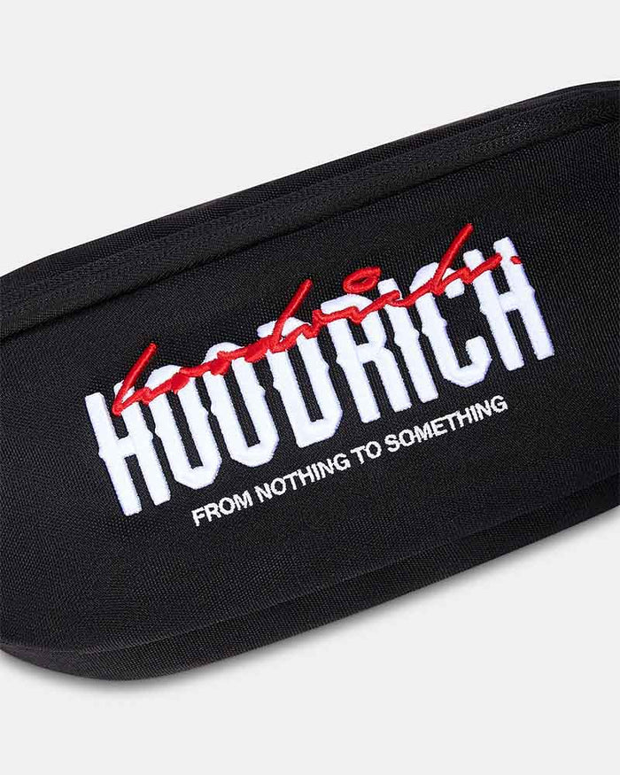 A black cross body bag with a wide, patterned black and red strap. The front features a bold white 'HOODRICH' logo with red graffiti-style lettering above it and smaller white text below reading 'FROM NOTHING TO SOMETHING'.