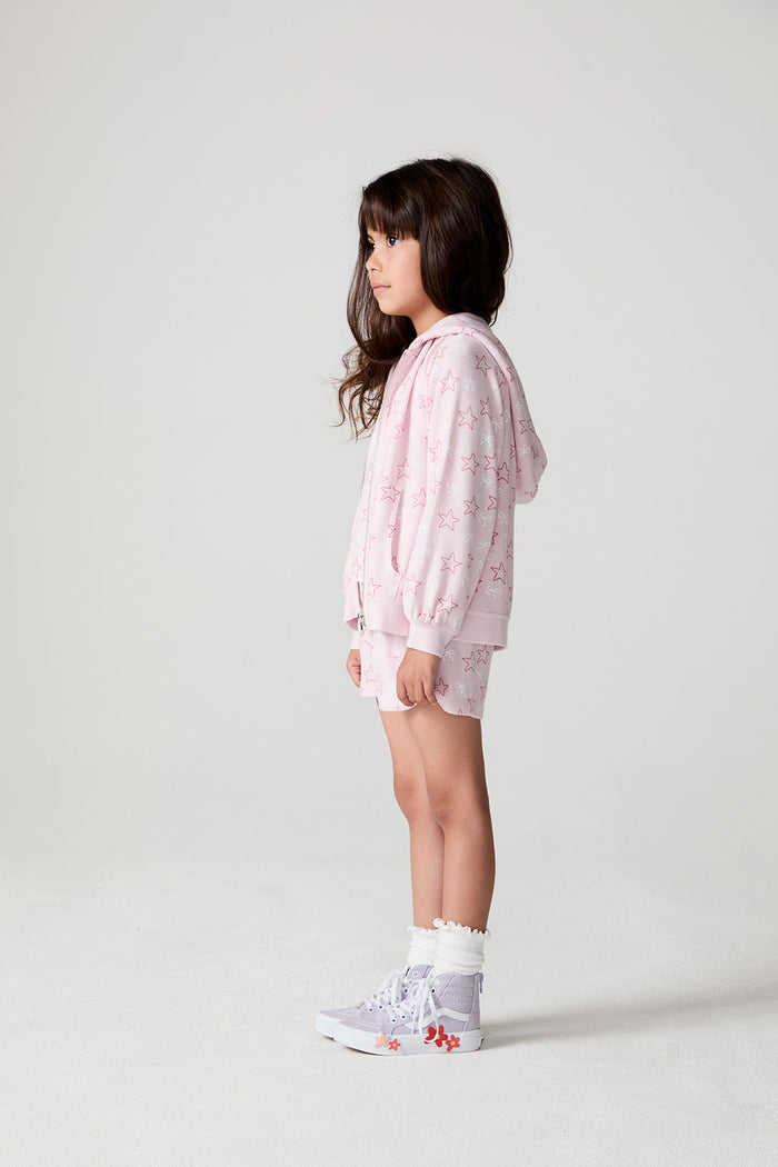 Side view of a girl wearing the Chaser Bows and Stars Zip-Up and shorts on a neutral background