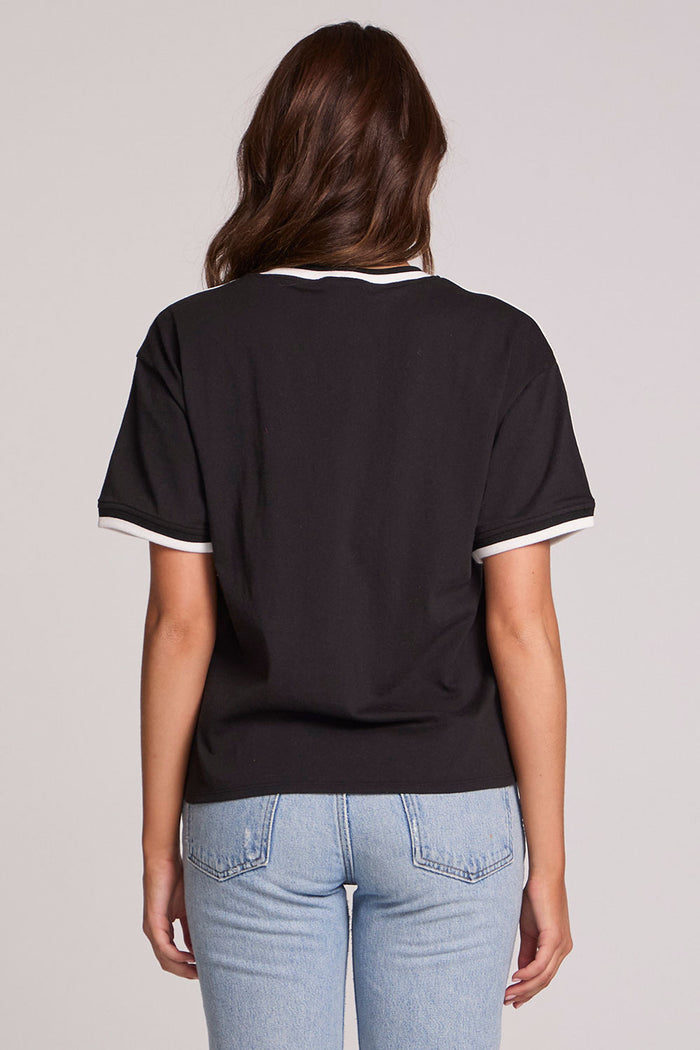 Back view of a woman wearing the Chaser Brooklyn Varsity Graphic Tee on a neutral background with hands at sides