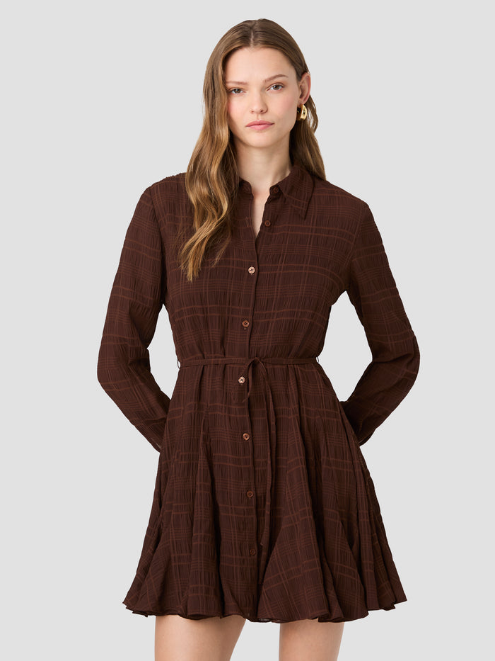 A woman wearing a brown mini length Shirt dress with a checked pattern, long sleeves, pointed collar, button through fastening, selfie tie waistband and a flared skirt.