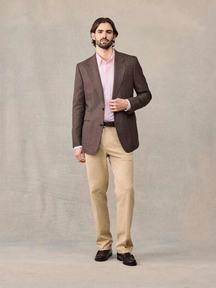 Man in a brown plaid sportcoat buttoning the jacket, tan trousers and brown belt visible.